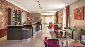 Un moderno vestíbulo de hotel con un mostrador de recepción curvo, zona de estar con sofás y sillones, un bar con cubero de vino y obras de arte en las paredes.