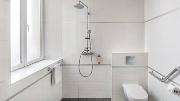 Une salle de bain moderne avec des carreaux blancs, une douche, des toilettes et une fenêtre.