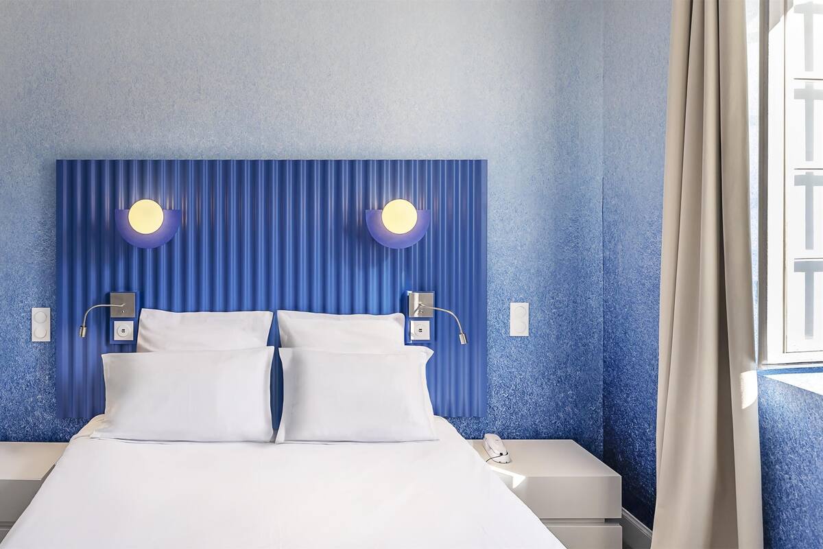 Una habitación de hotel moderna con una cama grande, dos mesitas de noche y un cabecero con iluminación integrada.