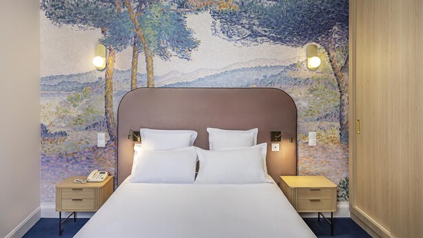 Ein Hotelzimmer mit einem großen Bett, zwei Nachttischen und einer Wand mit Landschaftsbild.