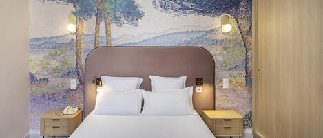 A hotel room with a large bed, two bedside tables, a nightstand, and a wall with a painted landscape.