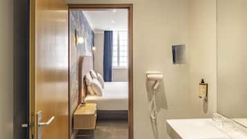 Una habitación de hotel con una cama, una tocador con espejo, un secador de pelo y un teléfono montado en la pared.