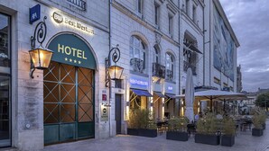 Ein Hotel mit großem Bogenportal, Außenbereich mit Sitzgelegenheiten und angrenzendem Restaurant.