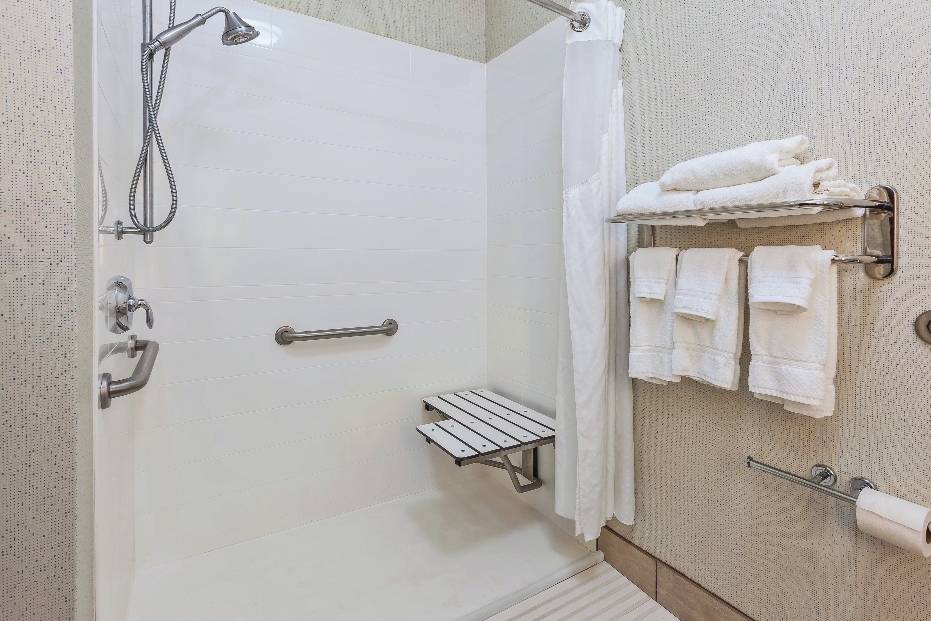 A shower area with a glass door, a towel rack with multiple towels, and a small shelf.