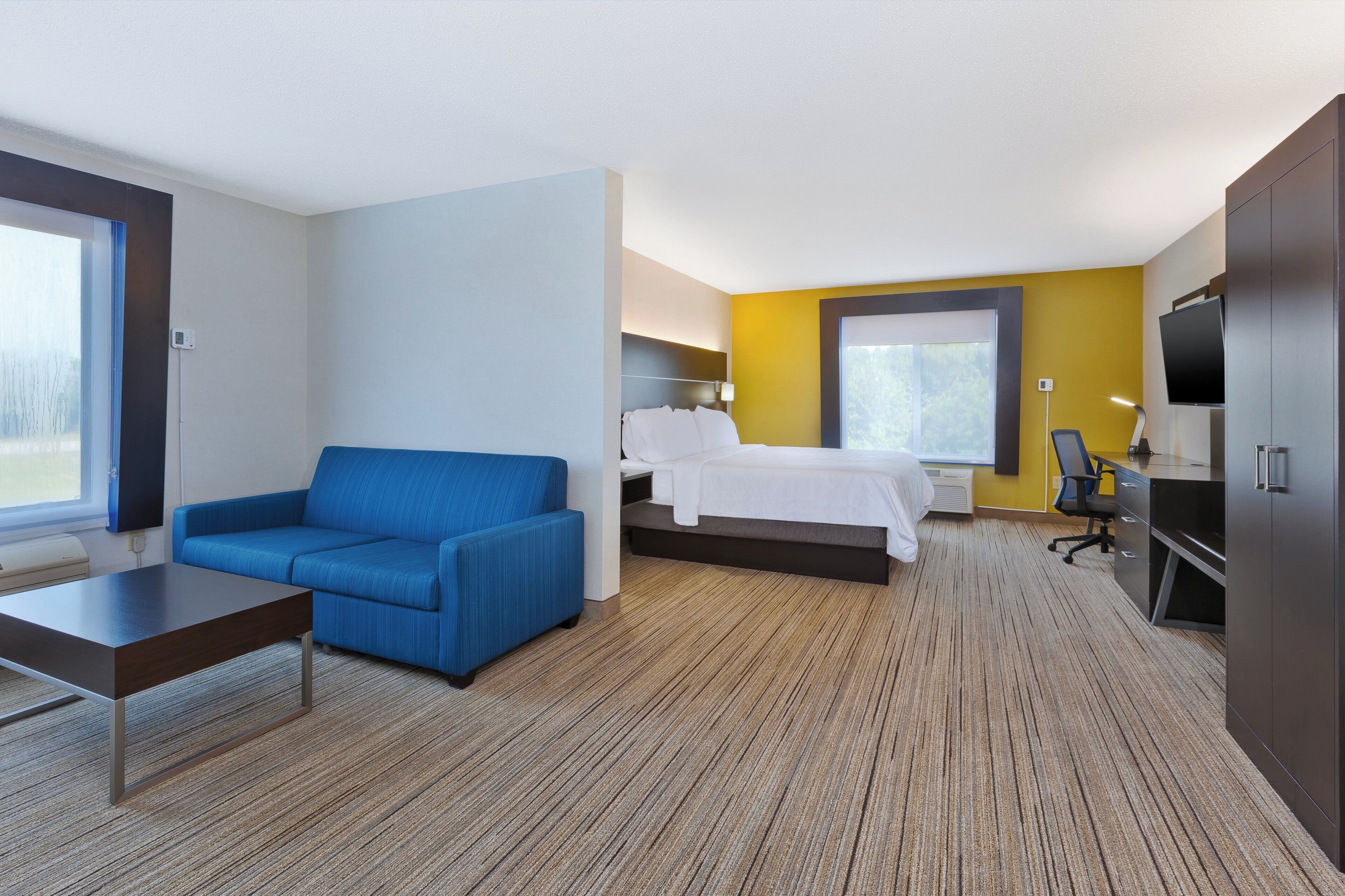 A hotel room with a bed, a blue sofa, a desk, a TV, and a wardrobe.