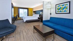 A hotel room with a bed, a blue sofa, a small table, a desk, and a chair.