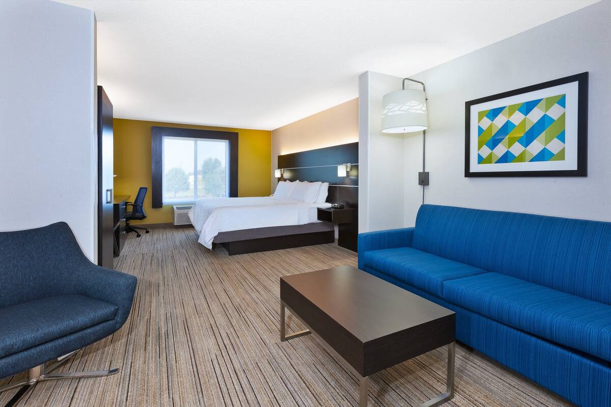 A hotel room with a bed, a blue sofa, a small table, a desk, and a chair.