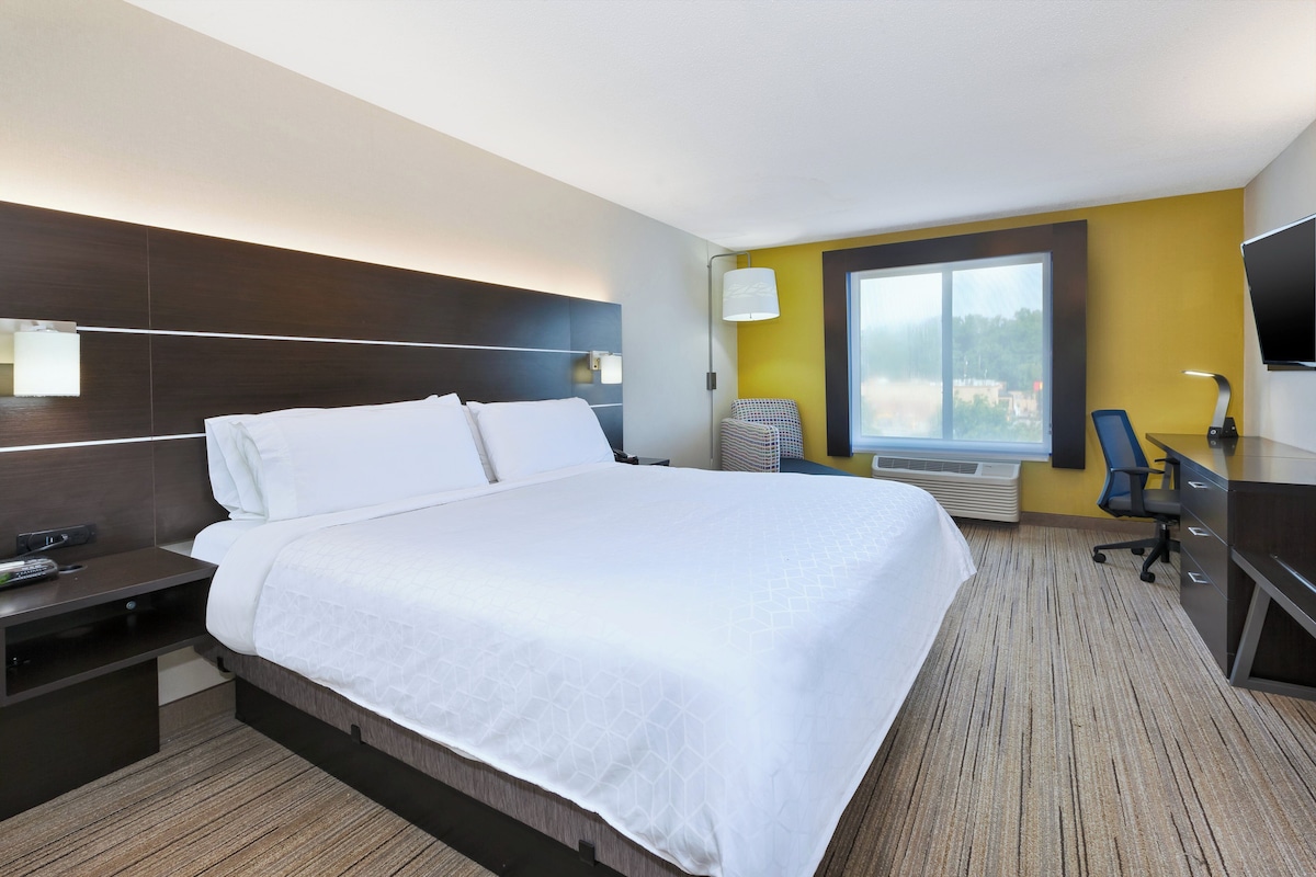 Habitación de hotel con una cama grande, un escritorio, una silla, un televisor y una ventana.