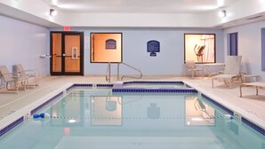 A swimming pool with lounge chairs and a sunbed, a door with an exit sign, and informational plaques on the walls.