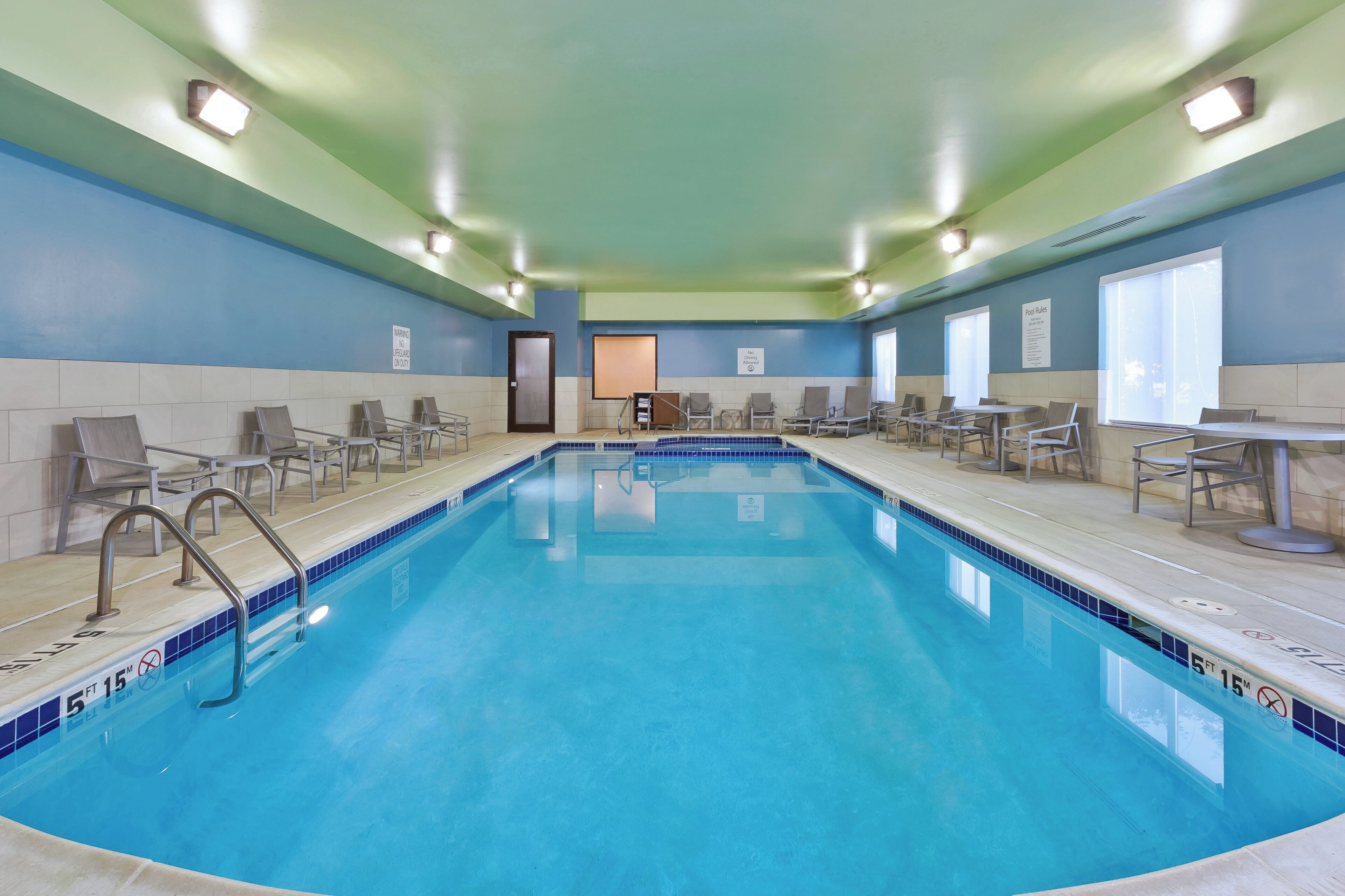 Une piscine intérieure d’une profondeur de 1,5 mètre sur 15 mètres de long, entourée de chaises longues et d’un espace aménagé au bord de la piscine, avec une porte et des fenêtres.