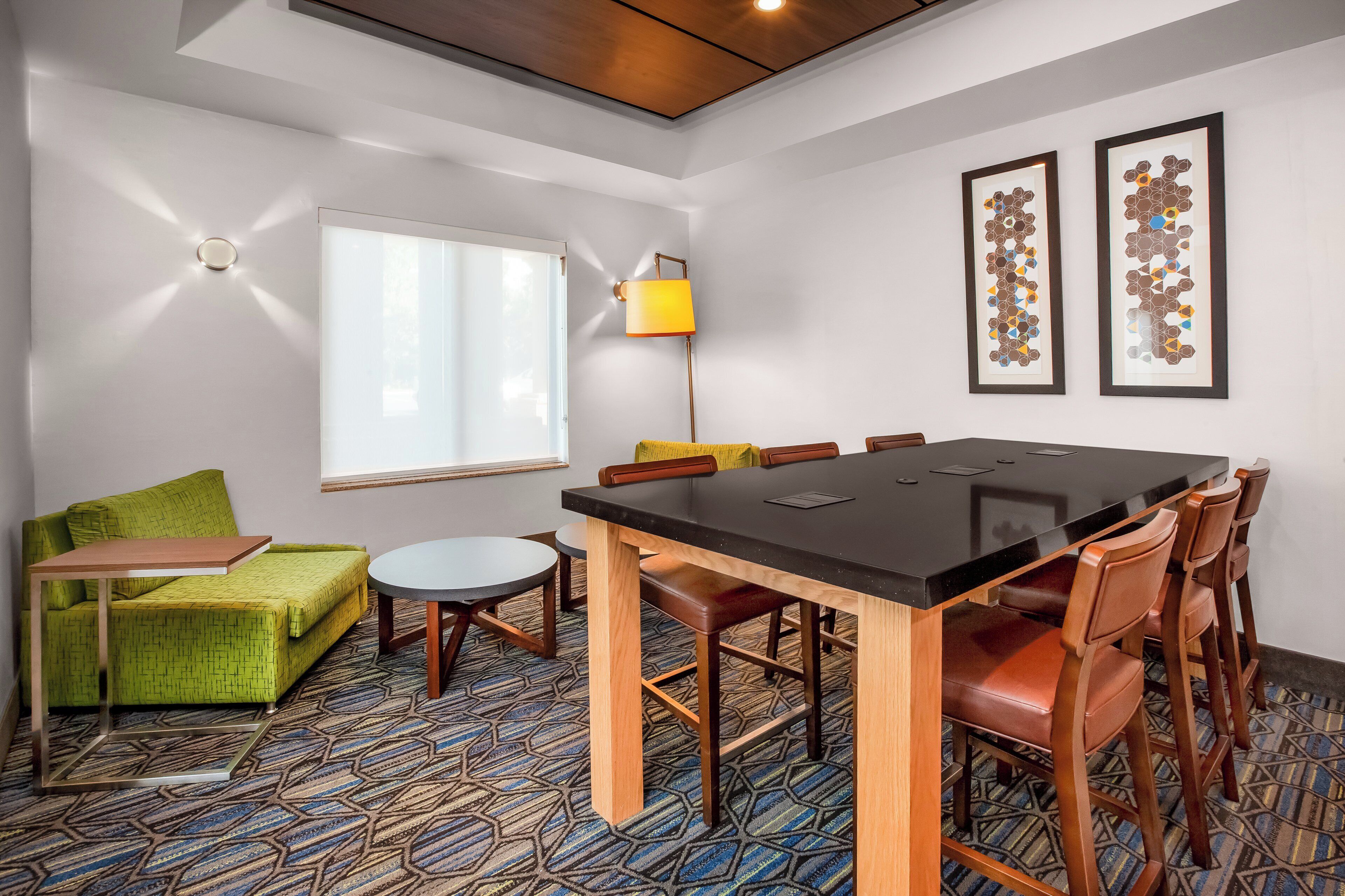 Een hotelkamer met een grote eettafel, een bank, een klein rond tafeltje en een lamp.