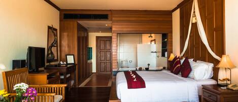 Una habitación de hotel con cama, mesita de noche, lámpara, silla, escritorio, televisor y un florero con flores.