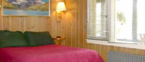 A room with a bed, a painting, a lamp, and a window.