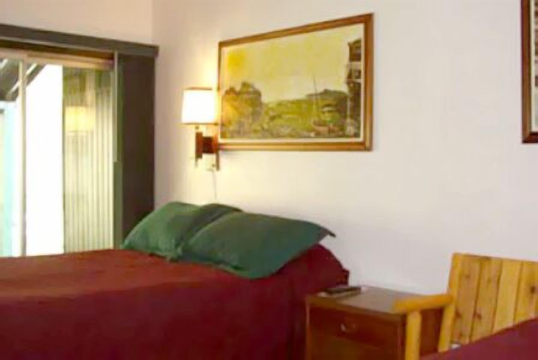A hotel room with a bed, a nightstand, a lamp, and a painting on the wall.