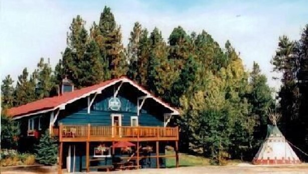 Une maison à deux étages, avec un toit rouge et un balcon, entourée d’une forêt dense.
