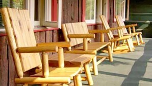 Une rangée de fauteuils Adirondack en bois, avec une terrasse en bois et un bâtiment en bois doté de fenêtres en arrière-plan.