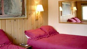 Une chambre avec deux lits, des murs en bois, un tableau et deux lampes fixées au mur.
