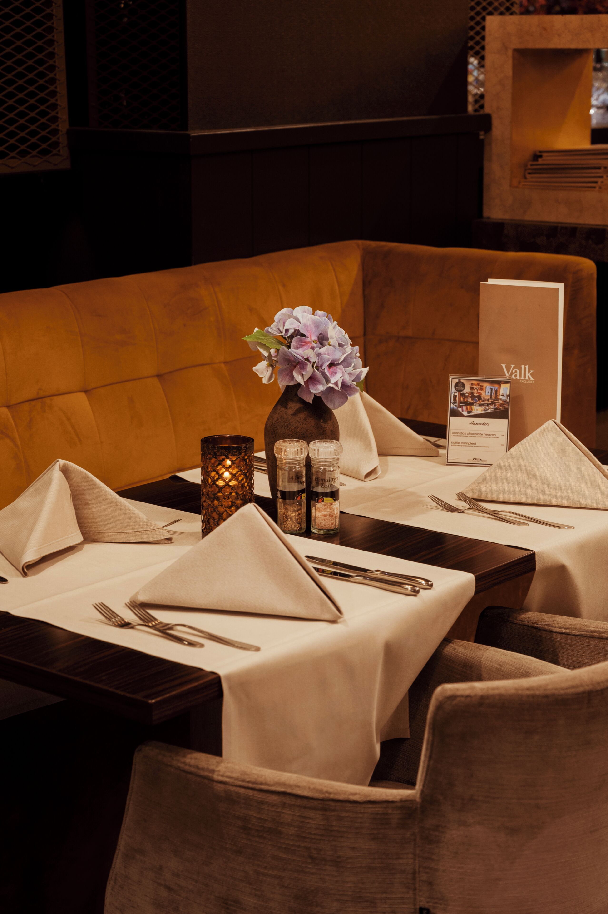 A dining table set with a vase of flowers, salt and pepper shakers, and a menu.