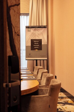Un salón de conferencias con una pantalla de presentación, una mesa de madera y varias sillas tapizadas.