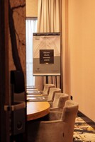 Une salle de conférence équipée d’un écran de présentation, d’une table en bois et de plusieurs fauteuils rembourrés.