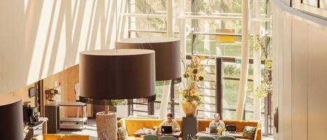 A spacious indoor area with multiple seating arrangements, including tables and chairs, and large windows allowing natural light.