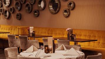 A dining area with round tables, chairs, and a yellow cushioned bench.