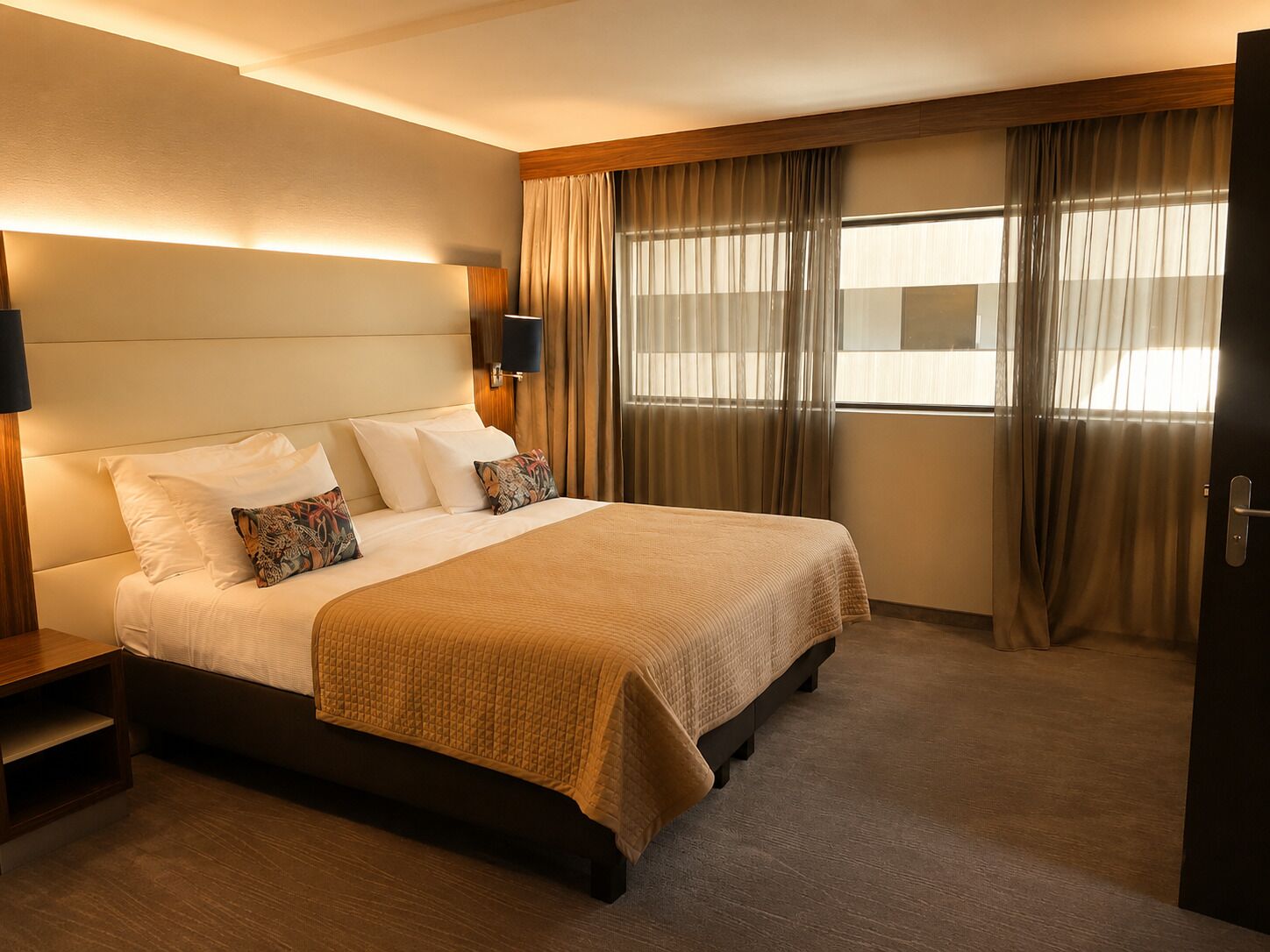 A hotel room with a large bed, a bedside table, a lamp, and a window with curtains.