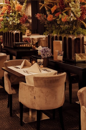 A restaurant setting with tables set for dining, featuring a variety of flowers in vases and candles on the tables. - Van der Valk Hotel Rotterdam - Blijdorp (Rotterdam)