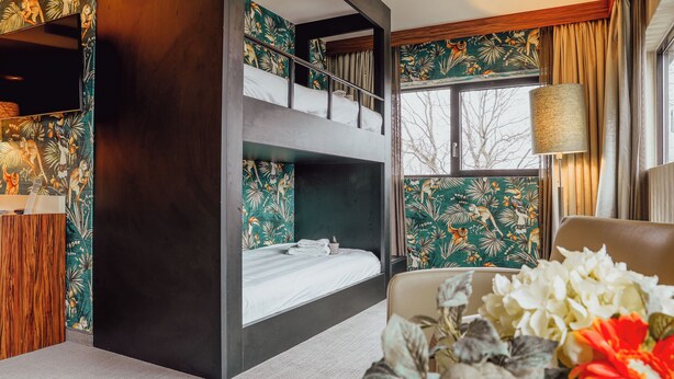 A room with a bunk bed, a desk, and a chair. There is a window with curtains, a lamp, and a vase with flowers. - Van der Valk Hotel Rotterdam - Blijdorp (Rotterdam)