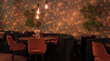 A cozy lounge area with a round table, two chairs, and a sofa. There are two hanging light fixtures above the table.