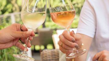 Two people toasting with wine glasses, a table with food and a wicker chair.