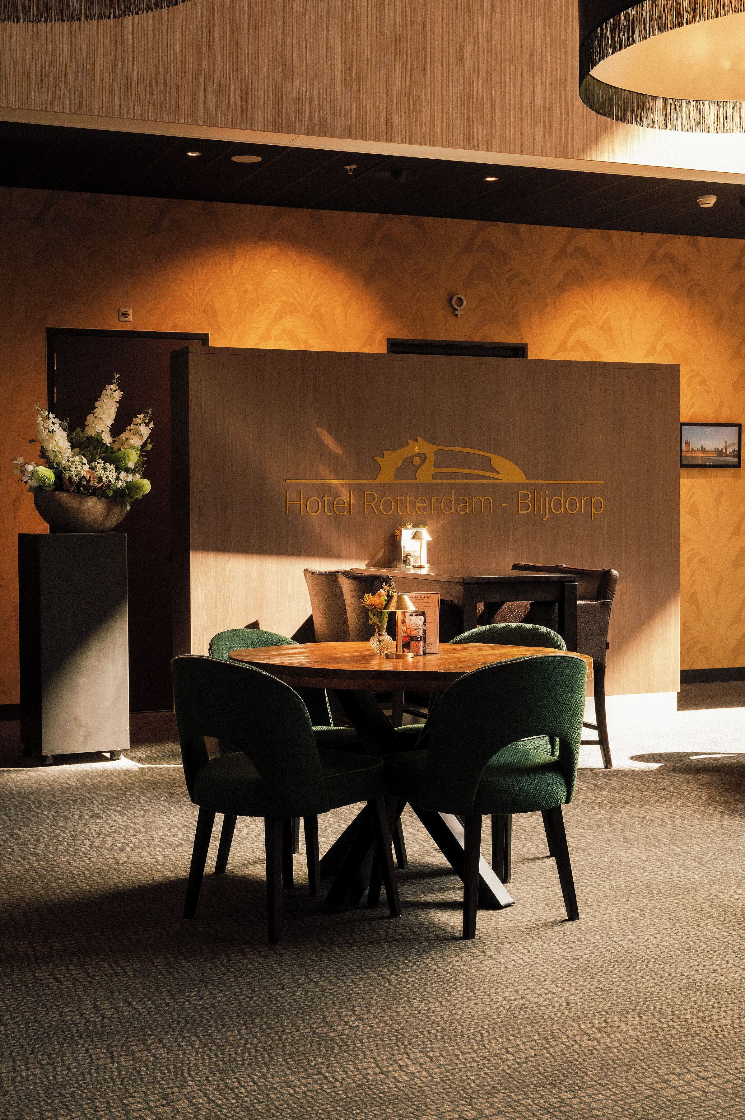 Un vestíbulo de hotel con mostrador de recepción, un arreglo floral y una zona de estar con sillas y una mesa.