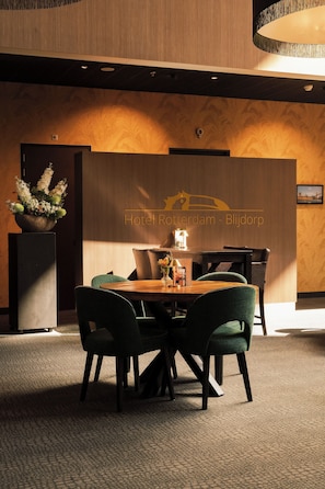 A hotel lobby with a reception desk, a flower arrangement, and a seating area with chairs and a table. - Van der Valk Hotel Rotterdam - Blijdorp (Rotterdam)