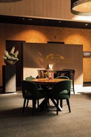 Un vestíbulo de hotel con mostrador de recepción, un arreglo floral y una zona de estar con sillas y una mesa.