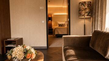 Hotelkamer met een bank, een kleintje tafeltje met bloemen, een bed met hoofdeinde, en een lamp met bloemendecoratie.