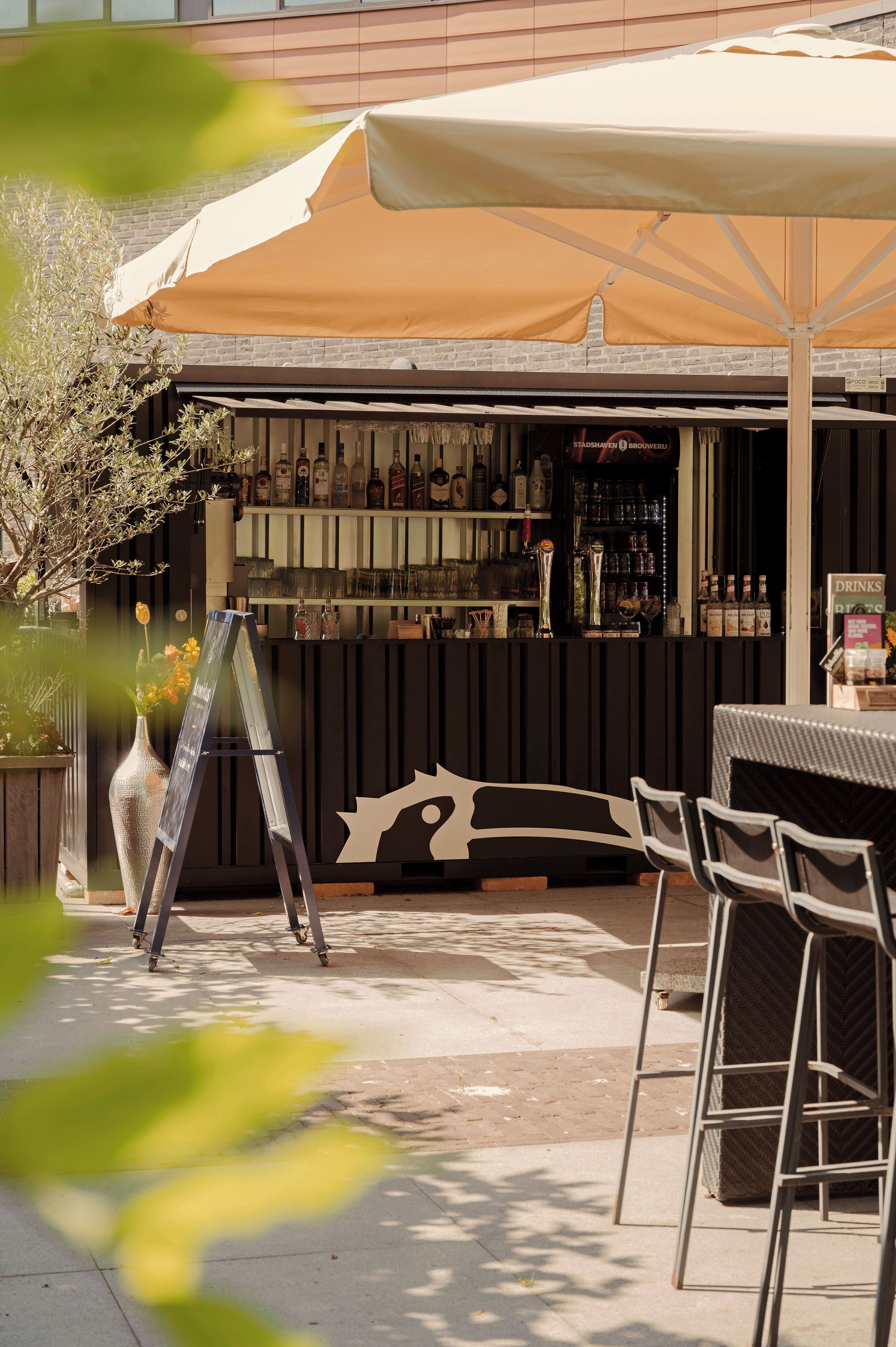 Un área de bar al aire libre con barra, distintas botellas y un conjunto de asientos.