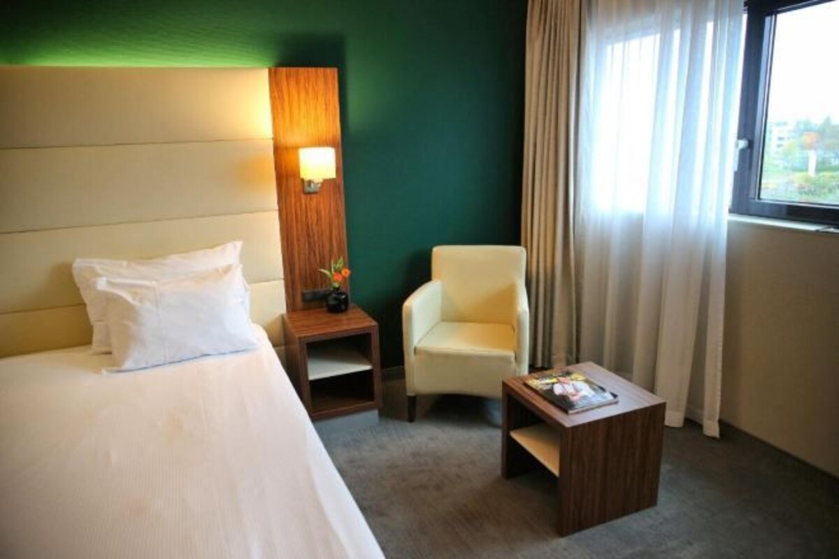 A hotel room with a bed, a chair, a nightstand, and a small table.