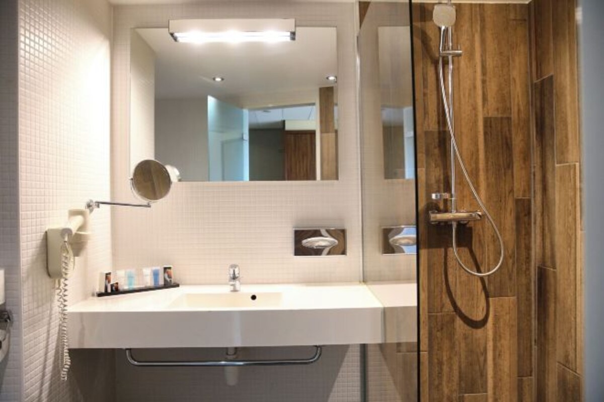 A modern bathroom with a white sink, a mirror, and a wooden shower enclosure.
