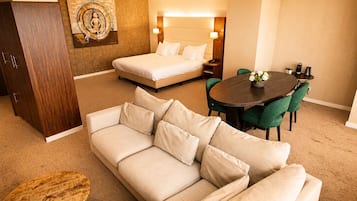 A hotel room with a bed, a sofa, a dining table with chairs, a small round table, and a wall-mounted artwork.