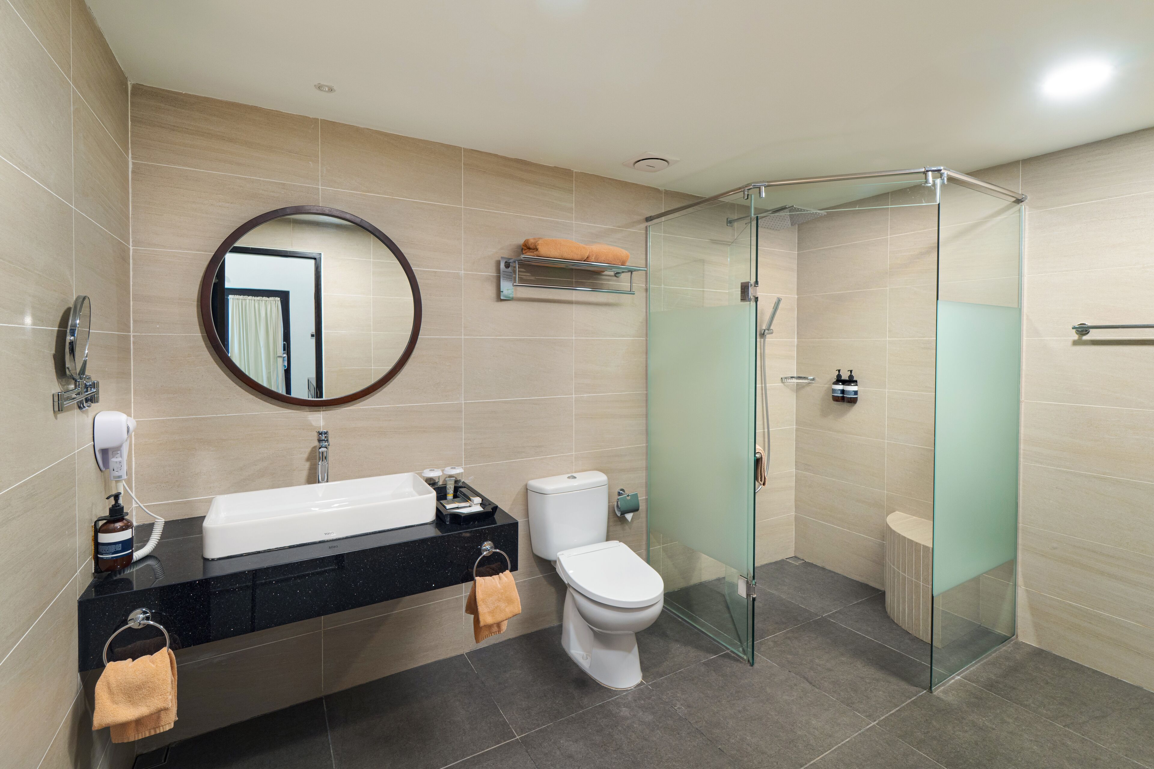 A modern bathroom with a glass-enclosed shower, a round mirror, a sink, and a toilet.