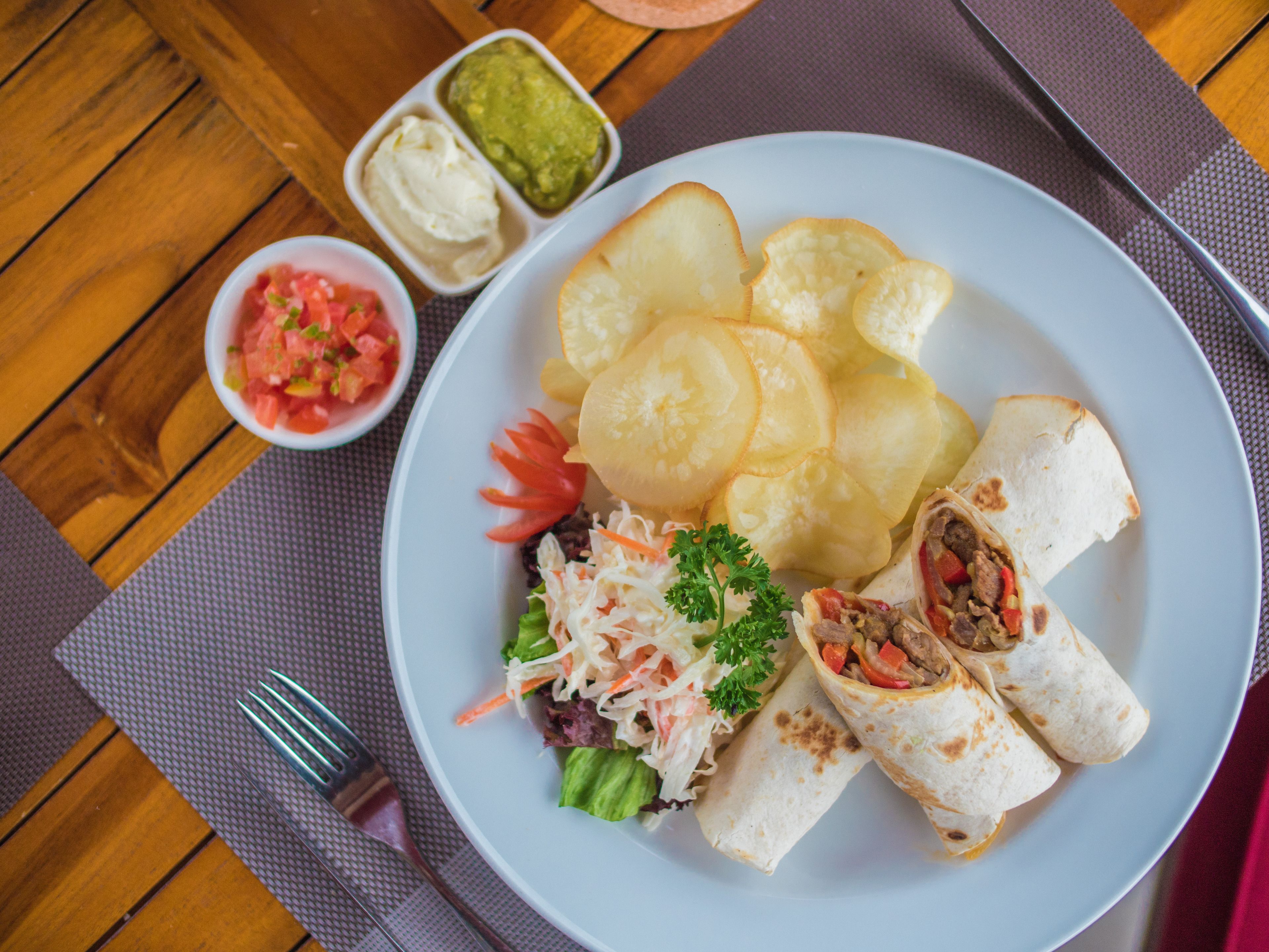 Un plato con un wrap, papas fritas y una ensalada pequeña.