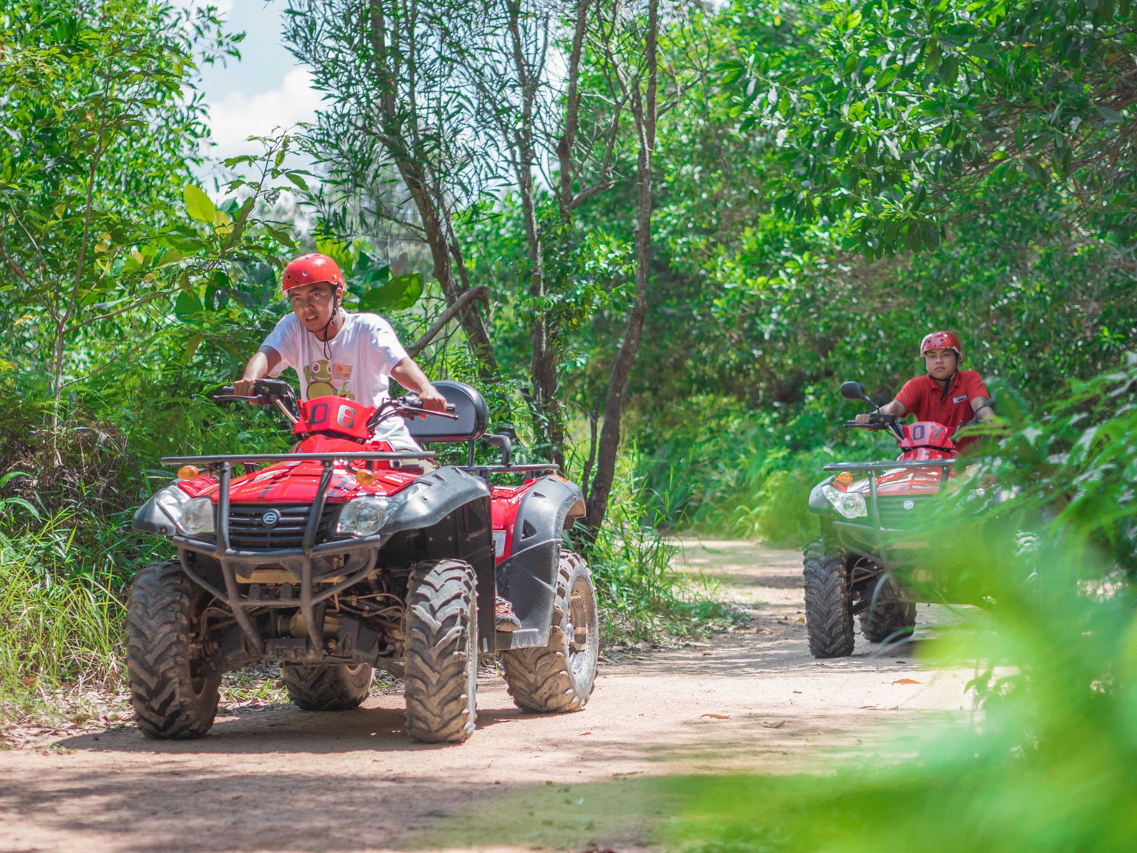 Two people riding ATVs on a dirt path surrounded by greenery.