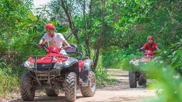 Two people riding ATVs on a dirt path surrounded by greenery.