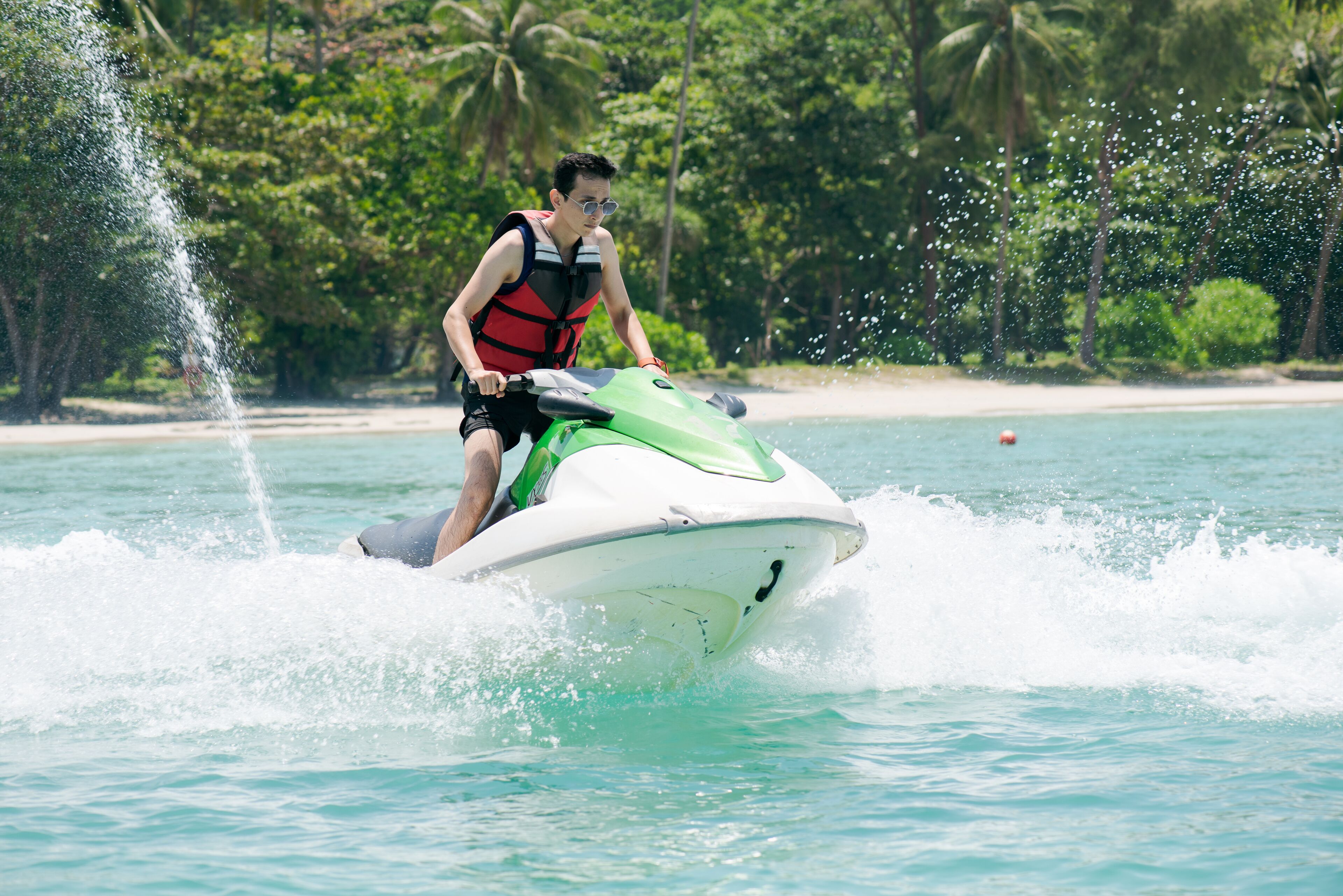 A person riding a jet ski on a body of water with a beach and palm trees in the background.
