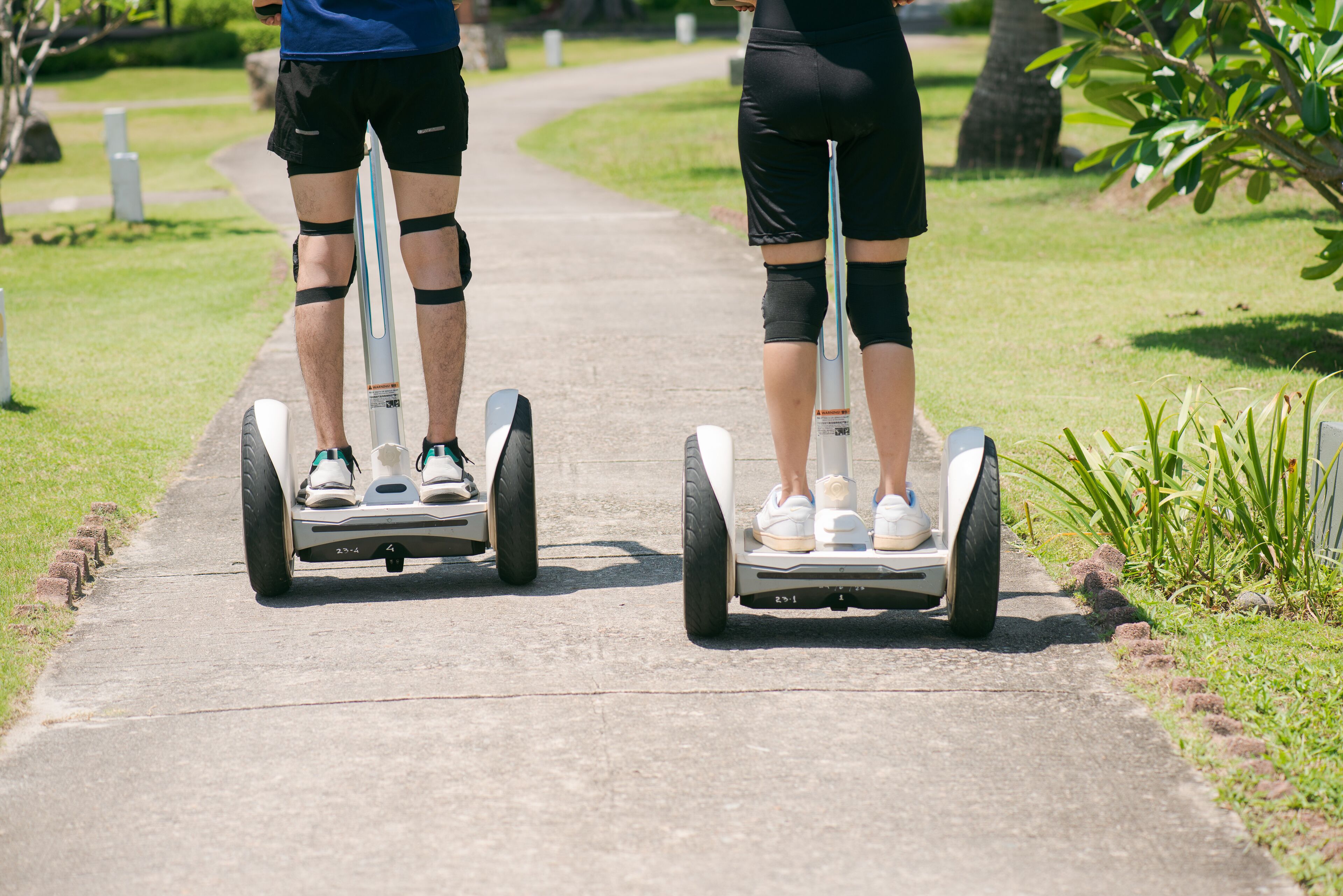 Two people on segways on a paved path in a park.