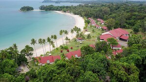 Un resort con acceso a la playa, palmeras y edificios de techo rojo.