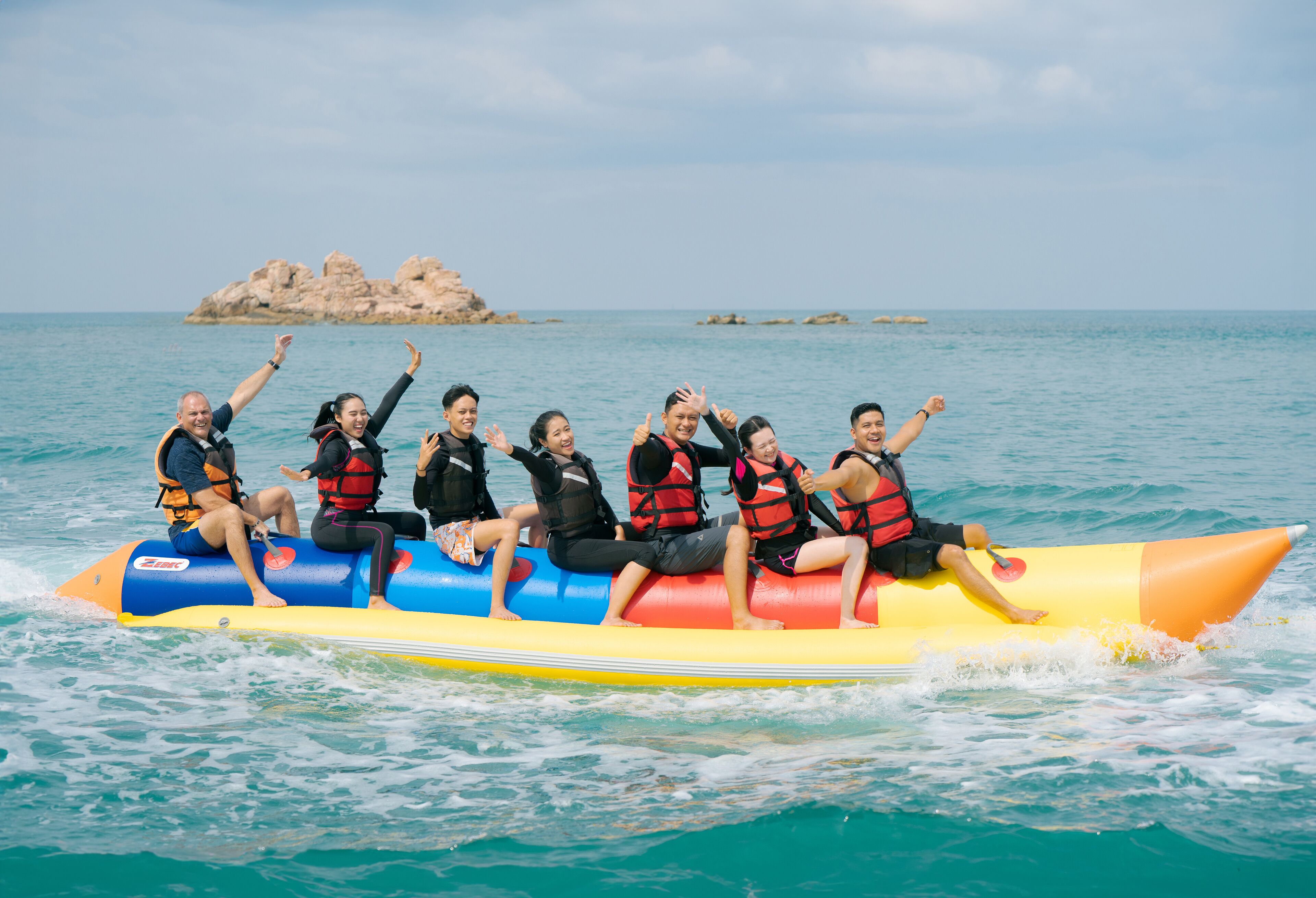 Un grupo de personas en un bote inflable colorido en el océano, con una isla rocosa al fondo.