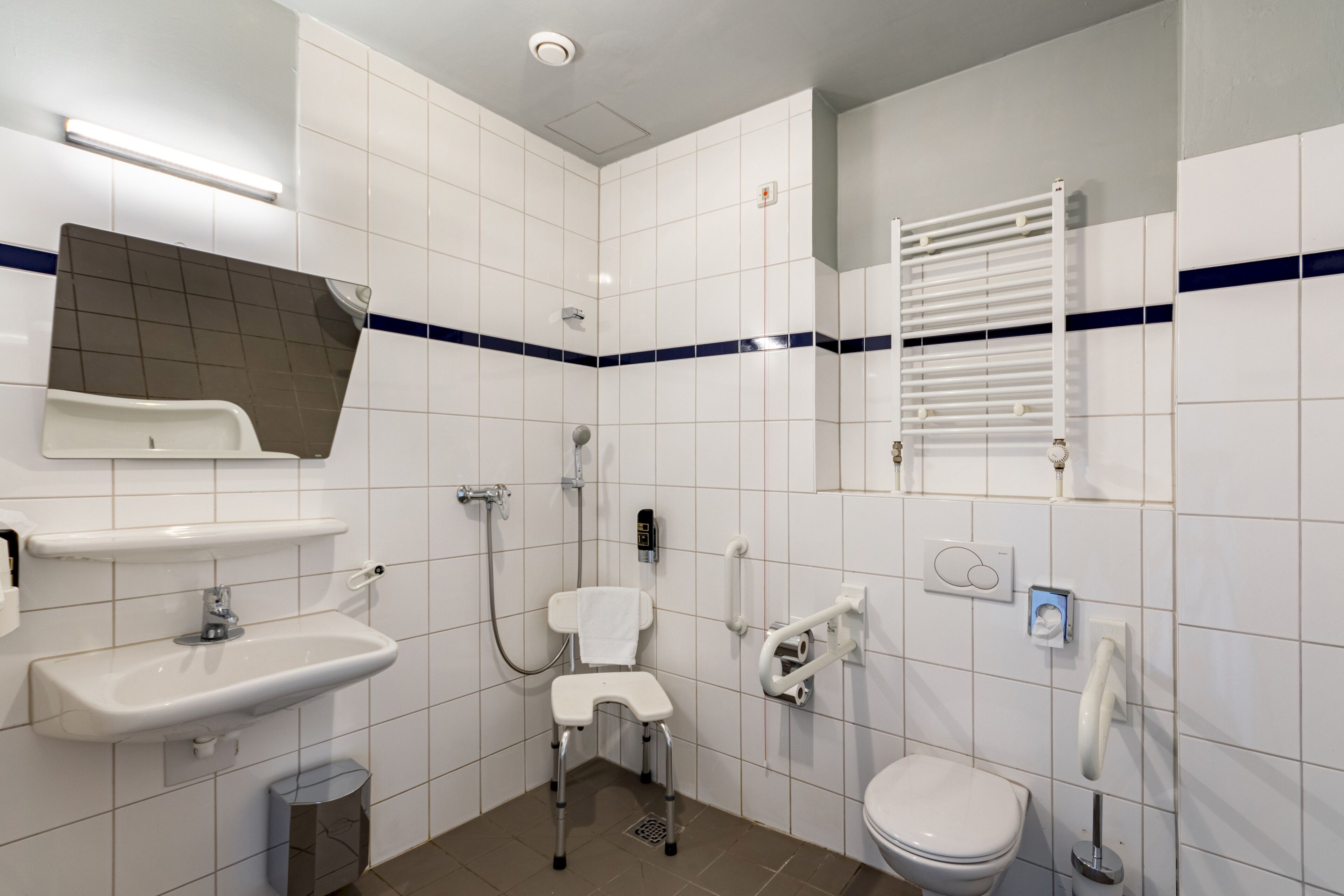 Un baño moderno con azulejos blancos, un lavabo, un inodoro, una ducha y un perchero para toallas.