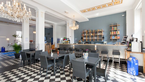 A hotel lobby with checkered flooring, a bar area with shelves of bottles, and a chandelier. - a&o Leipzig Hauptbahnhof (Leipzig)