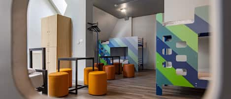 A modern interior with a bunk bed, orange ottomans, a wooden wardrobe, and a black metal table.
